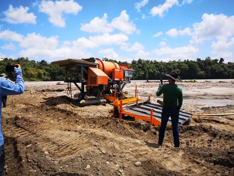 A Gold Screens NZ trommel screening plant operating beside a tropical river, two operators on site